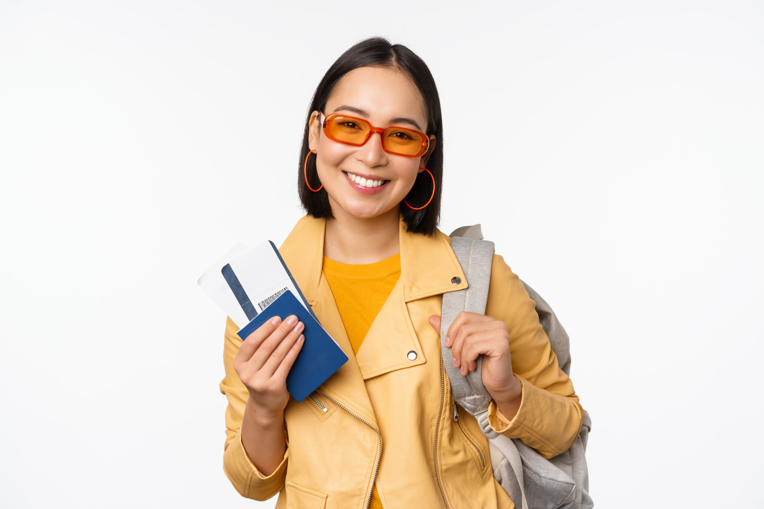 Happy asian girl going on vacation, holding passport and flight tickets, backpack on shoulder. Young woman tourist travelling abroad, standing over white background.